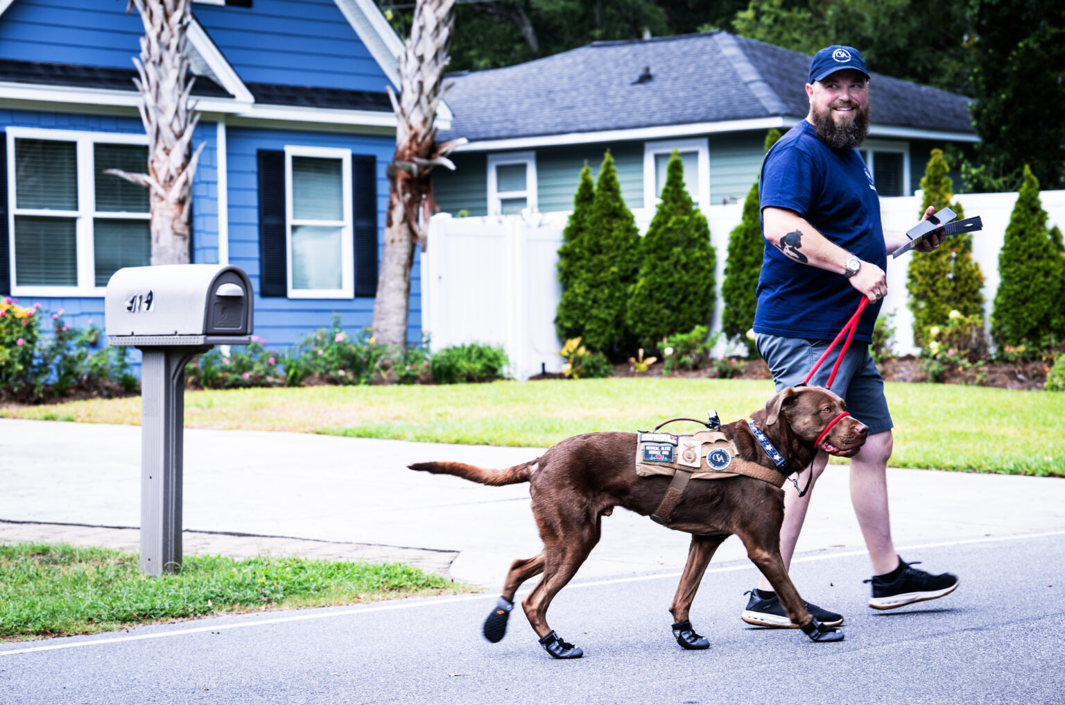 A picture of Robinson walking his service dog. They are near a blue house with a mailbox.