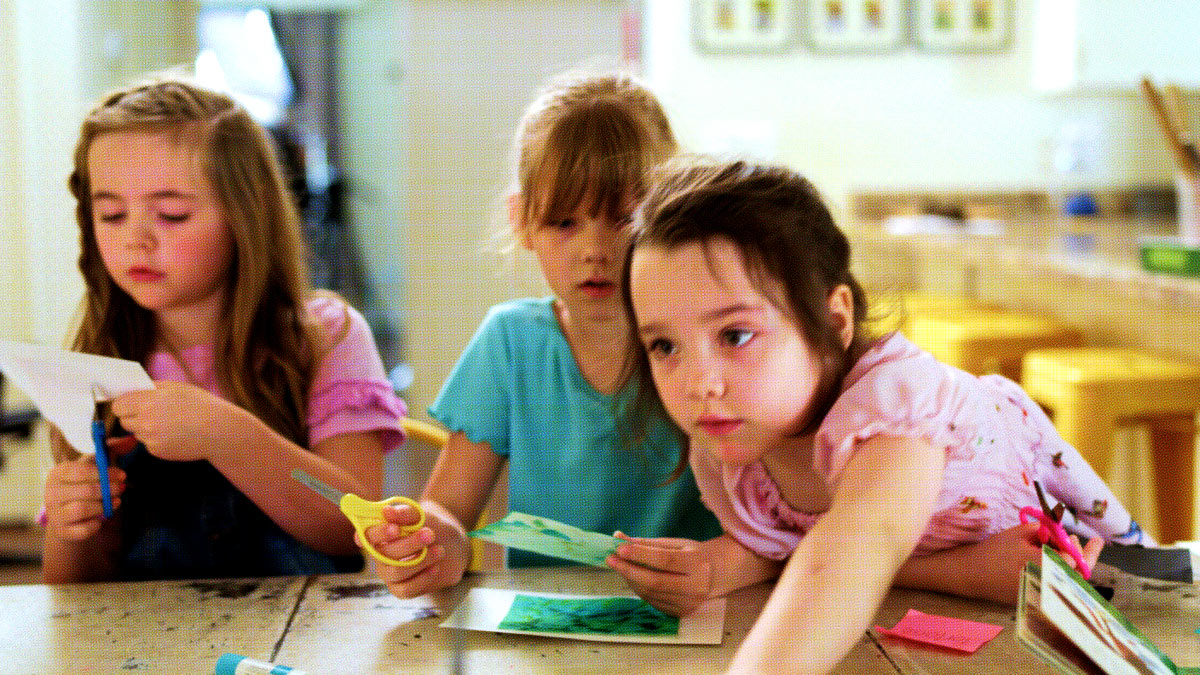 Three young girls at a school table cutting paper and engaged in learning