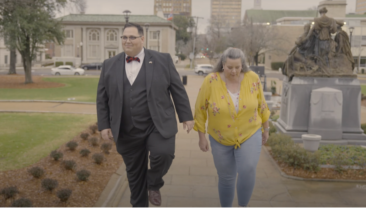 Cade Yates of Americans for Prosperity walks with Christi Berrong-Barber on a sidewalk