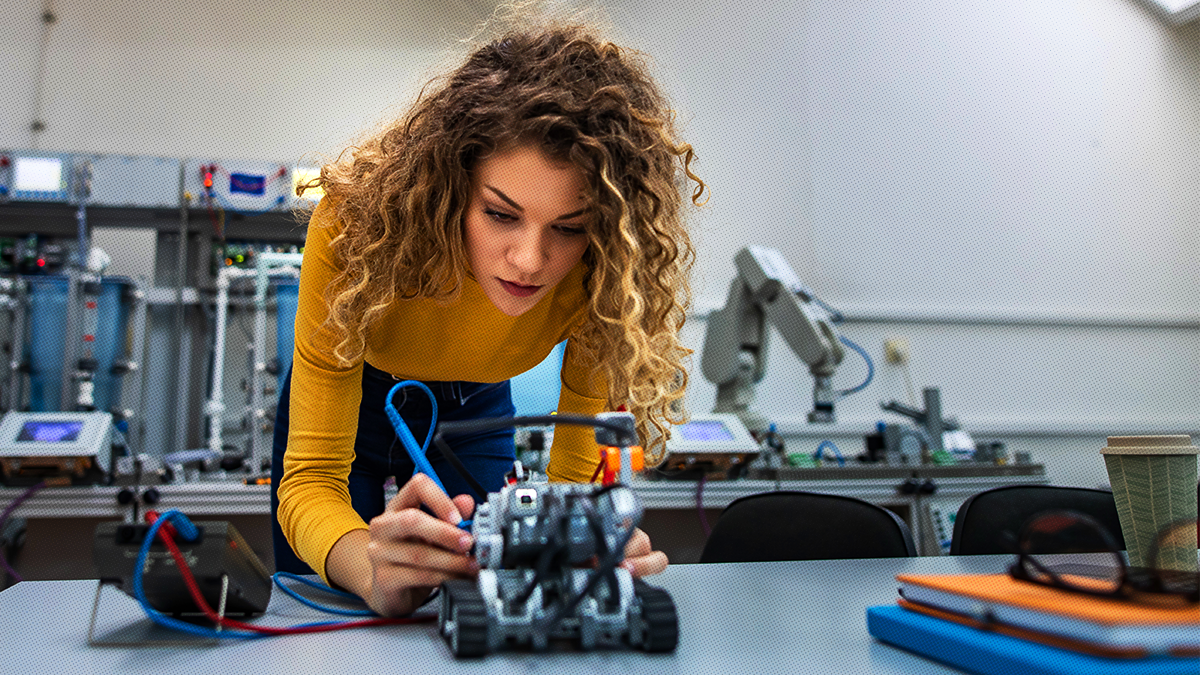 A woman with curly hair wearing a yellow sweater working on mechatronics 