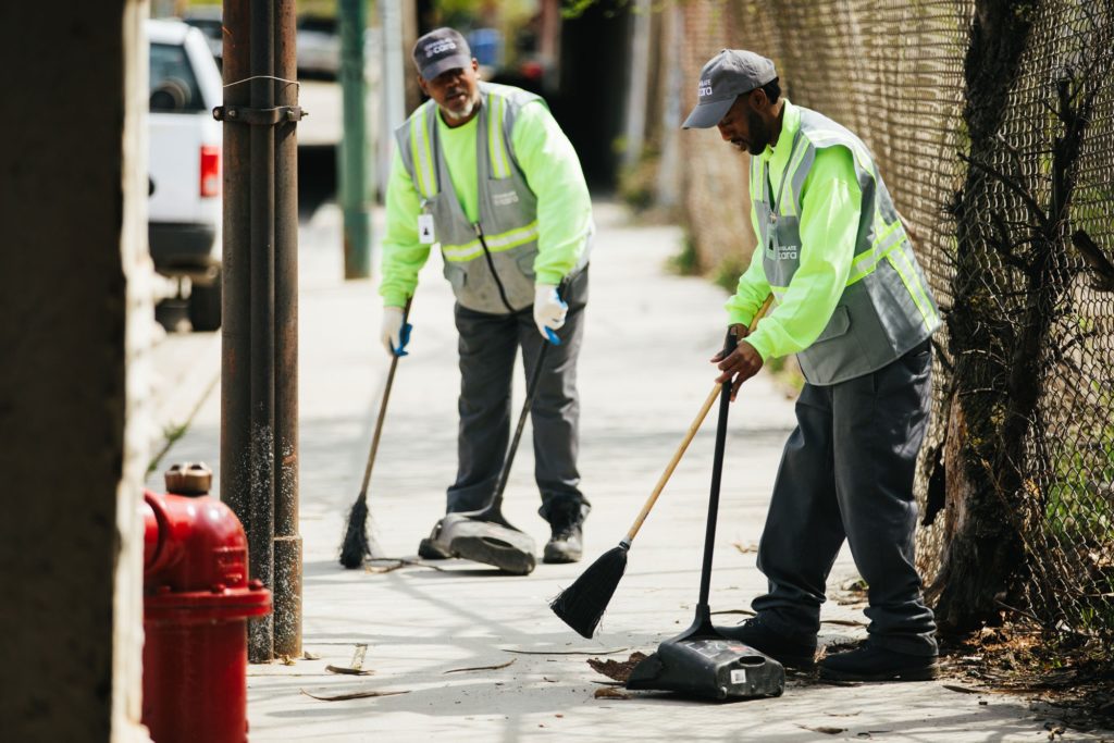 Cleanslate staff clean up a sidewalk with brooms