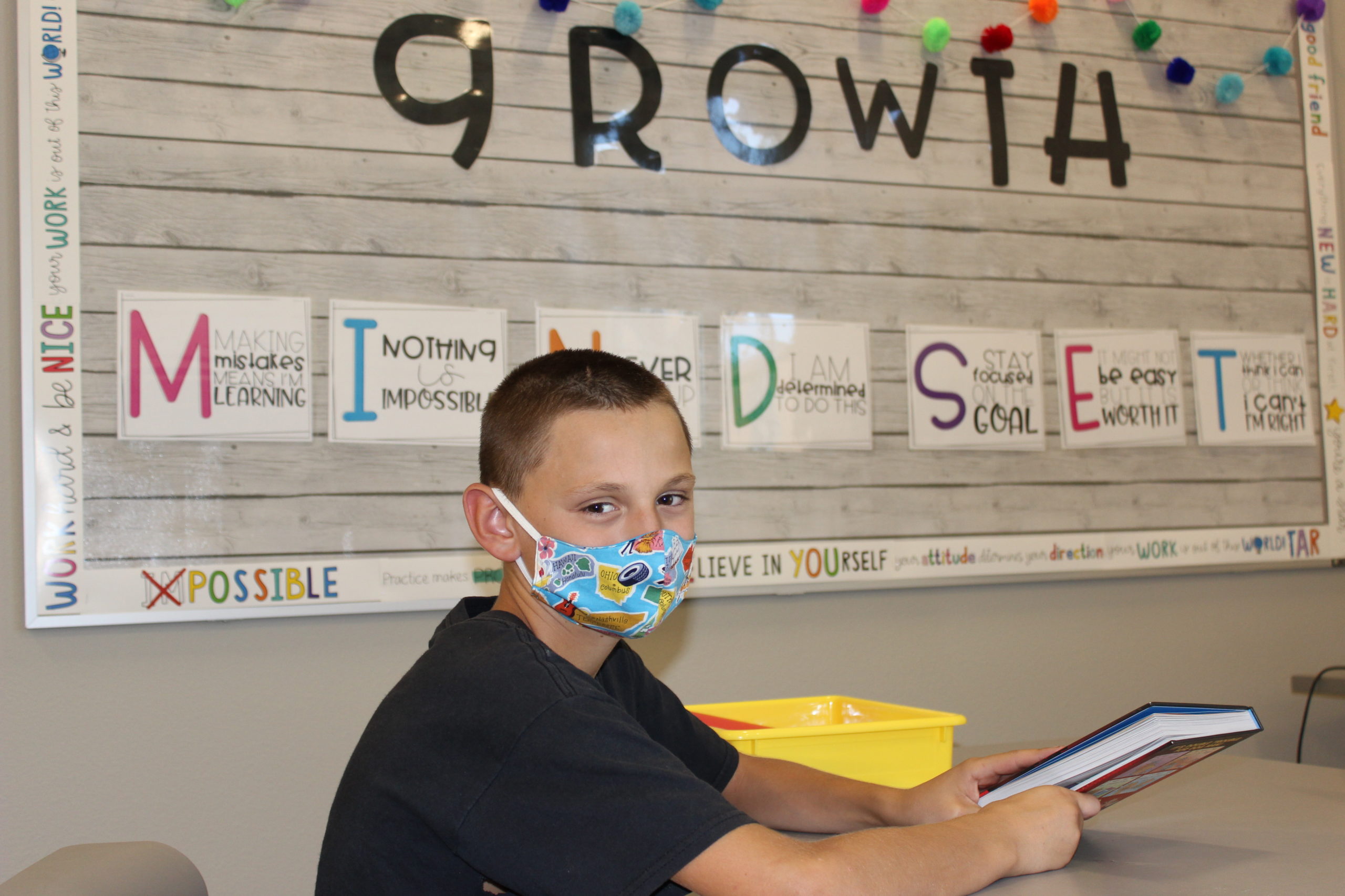 A child wearing a mask in school with a book in their hand