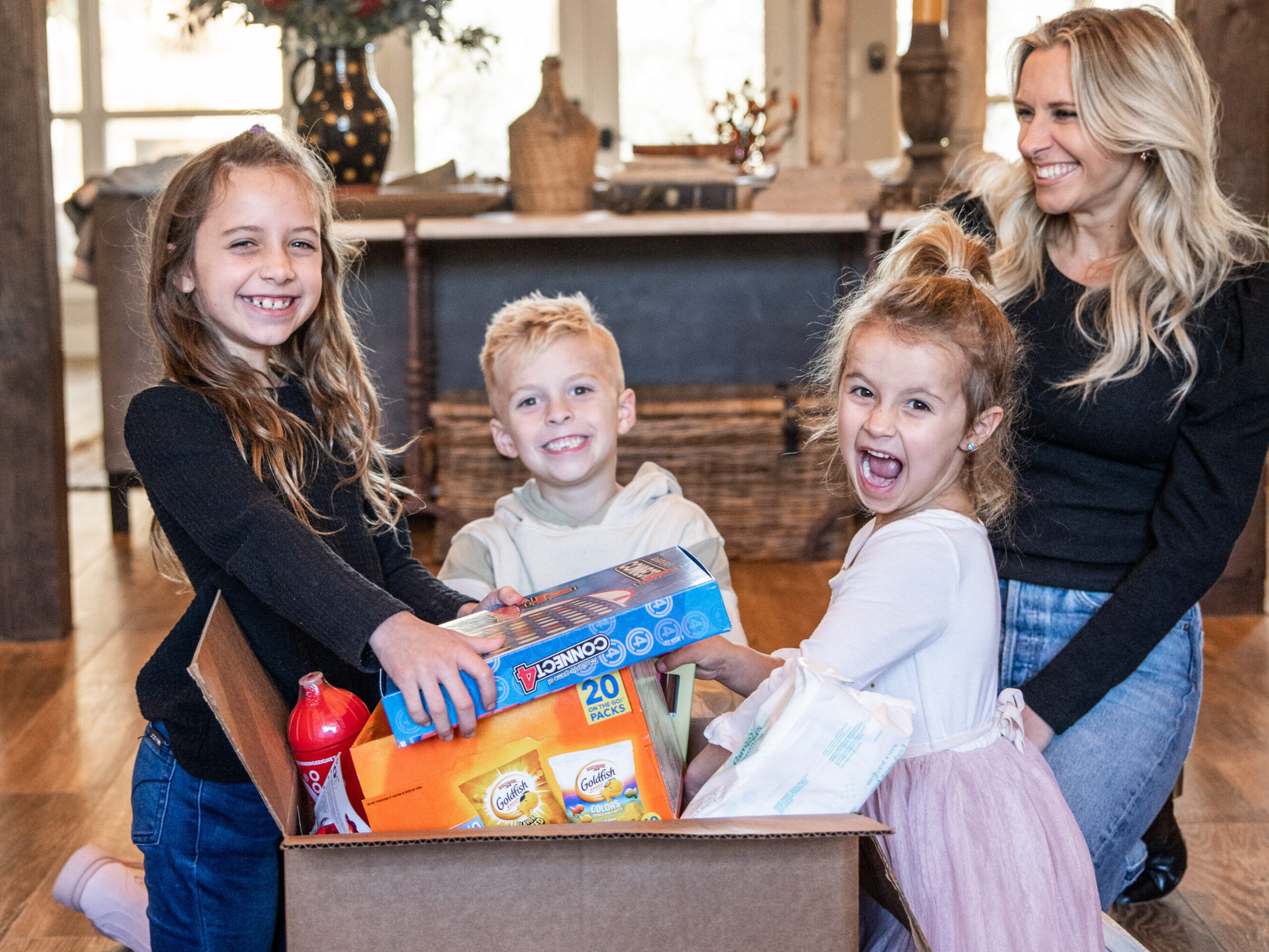 children and a women smiling for a photo as they take toys out of a box