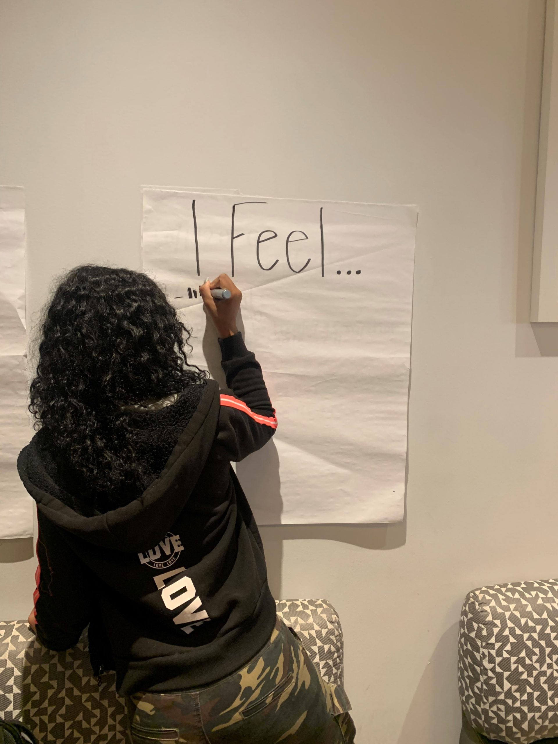 A person writes "I Feel" on a large sheet of paper on the wall