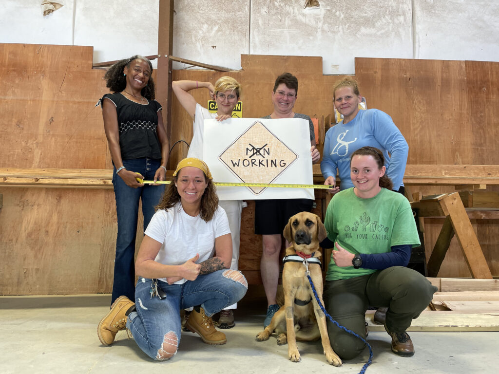 Hope Renovations trainees pose for a photo with a "working" sign and a dog