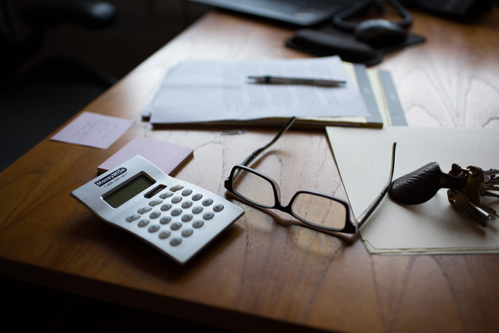 Miscellaneous items on a desk including a calculator, glasses, papers, and keys