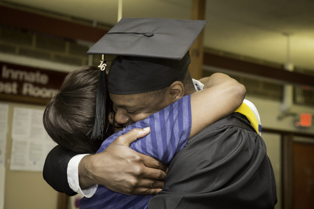 A man wearing a cap and gown hugs a woman