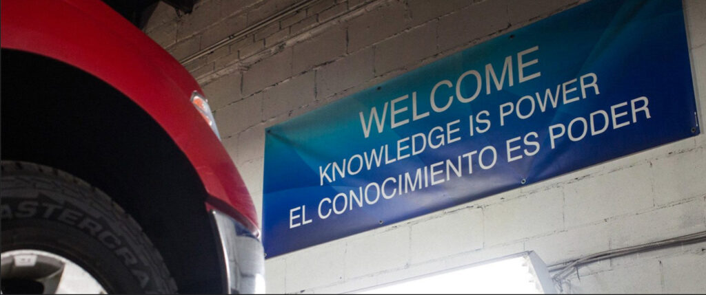 a welcome sign with Knowledge is Power written under it hung up on a wall in an auto shop