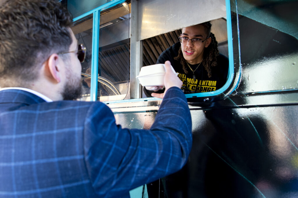 Man receiving a food container from a food truck worker.