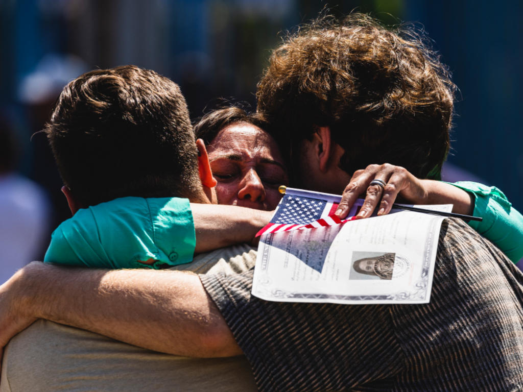 Three people sharing an emotional hug. The one in the middle holds a small American flag.