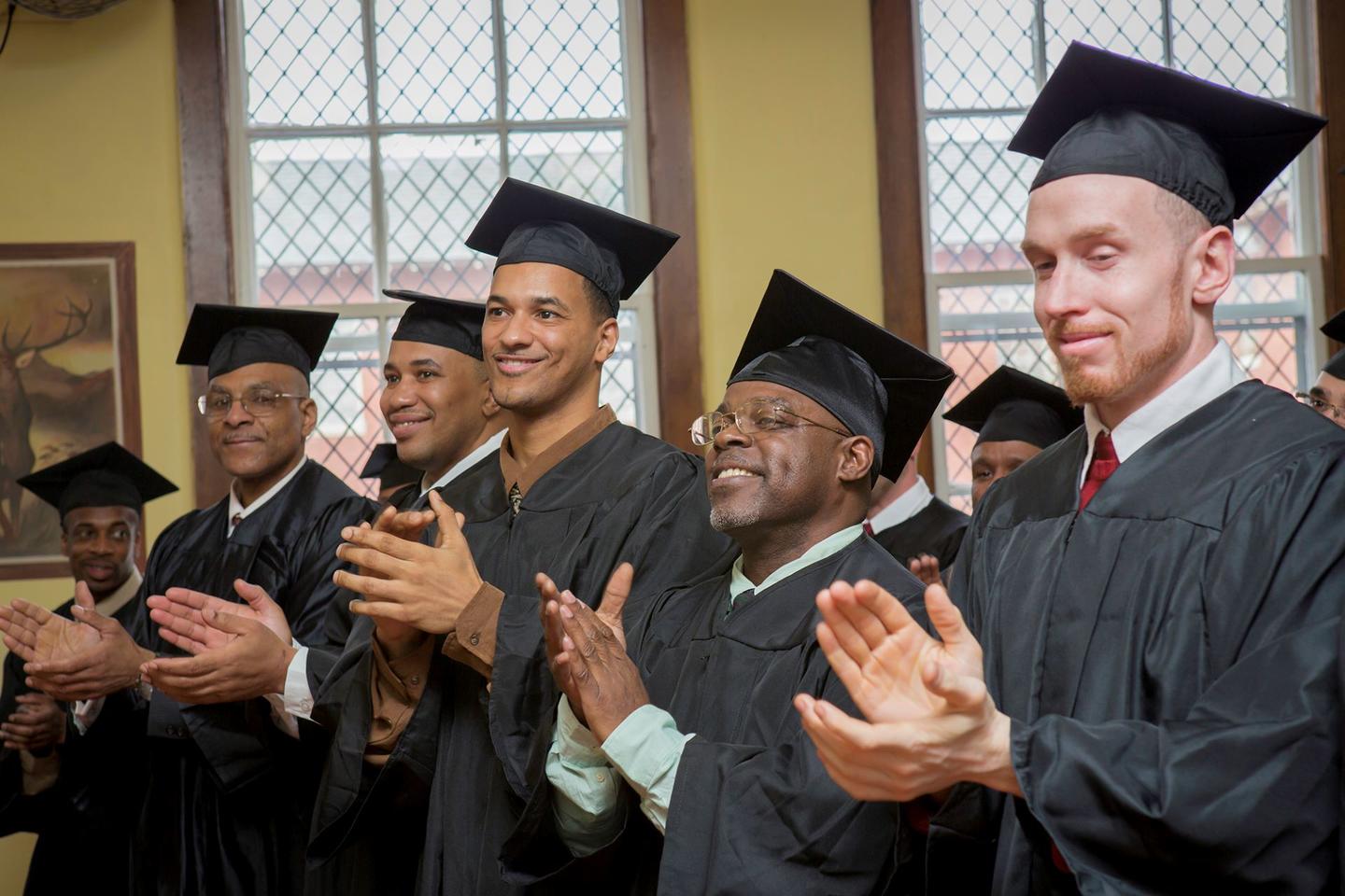 A group of men wearing caps and gowns clapping and smiling