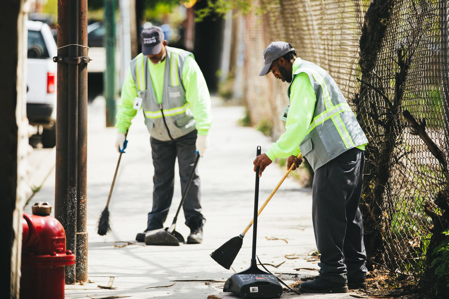 Two people cleaning up the street with brooms and dustpans