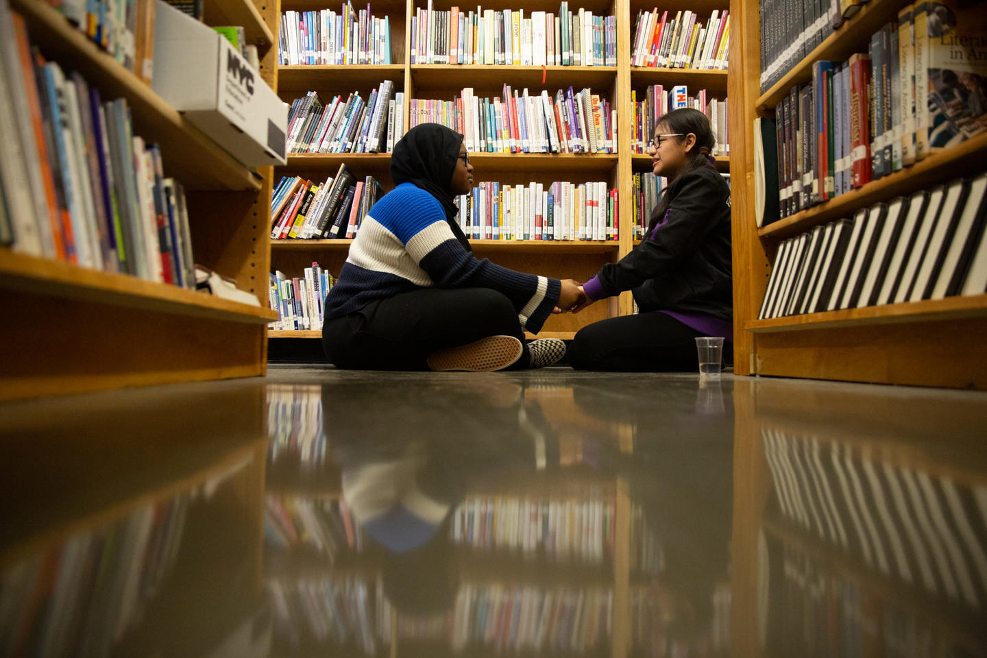 Two students sitting holding hands in a library