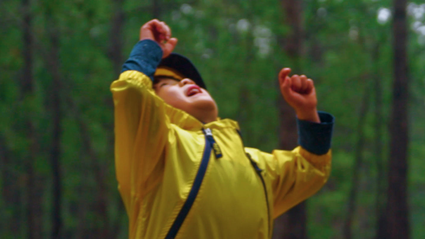 A child in a yellow windbreaker looks up at the sky