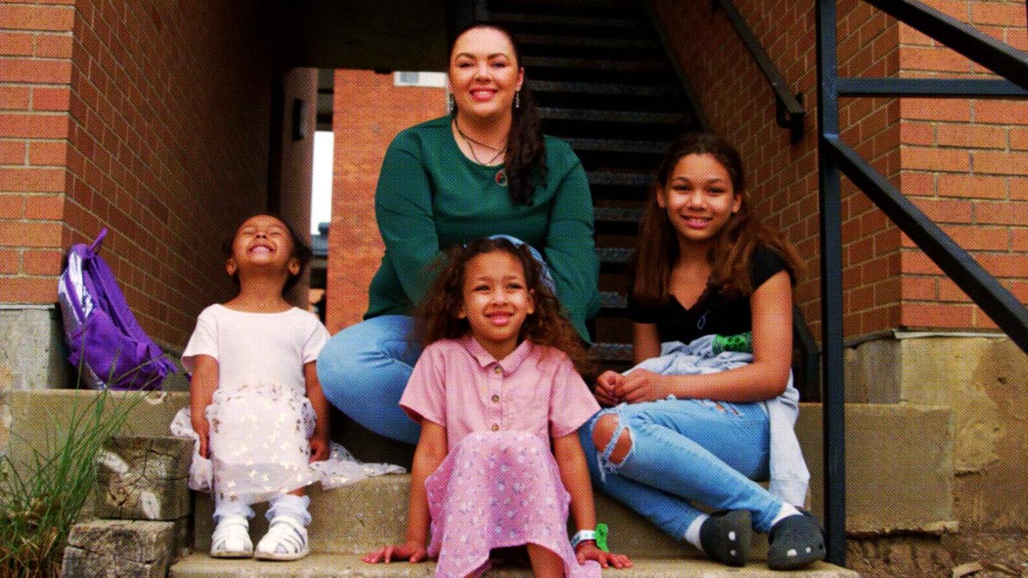 A woman in a green top sitting with three young girls on a set of concrete steps.