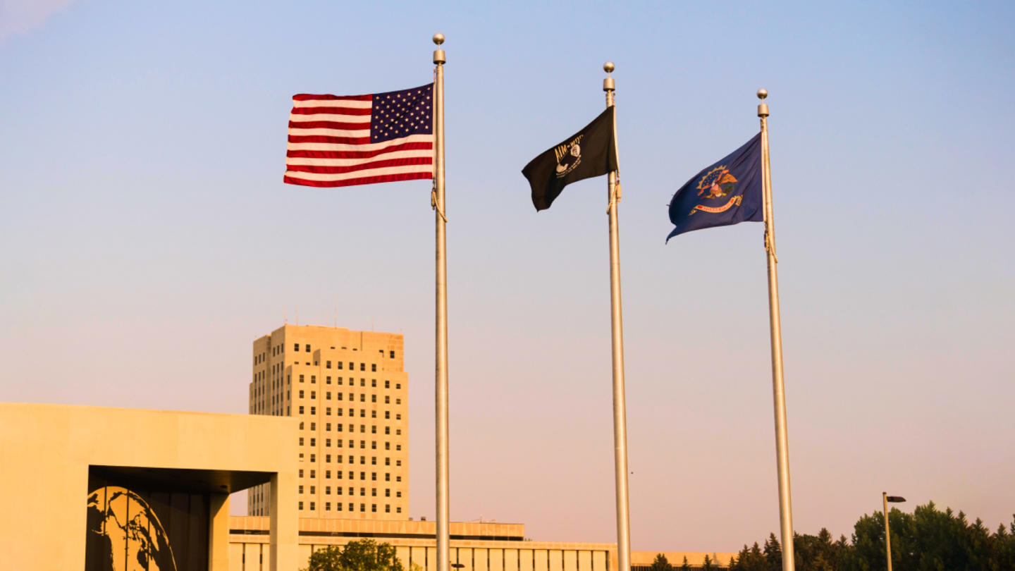 A shot of North Dakota's state capitol building, with three flags, including the U.S. and N.D. flags, in the foreground.