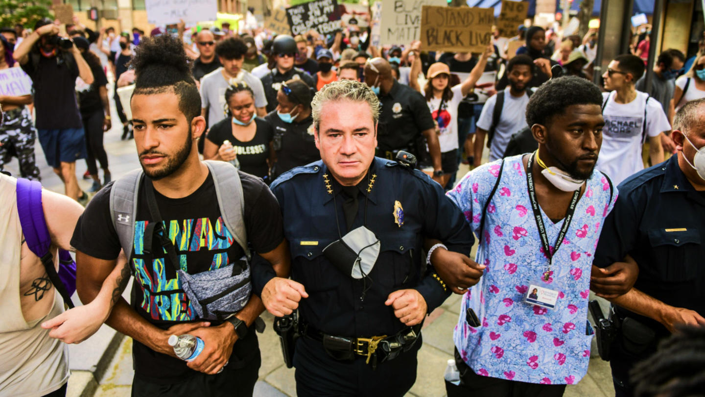 A protest where a police officer is linked arm in arm with someone in scrubs