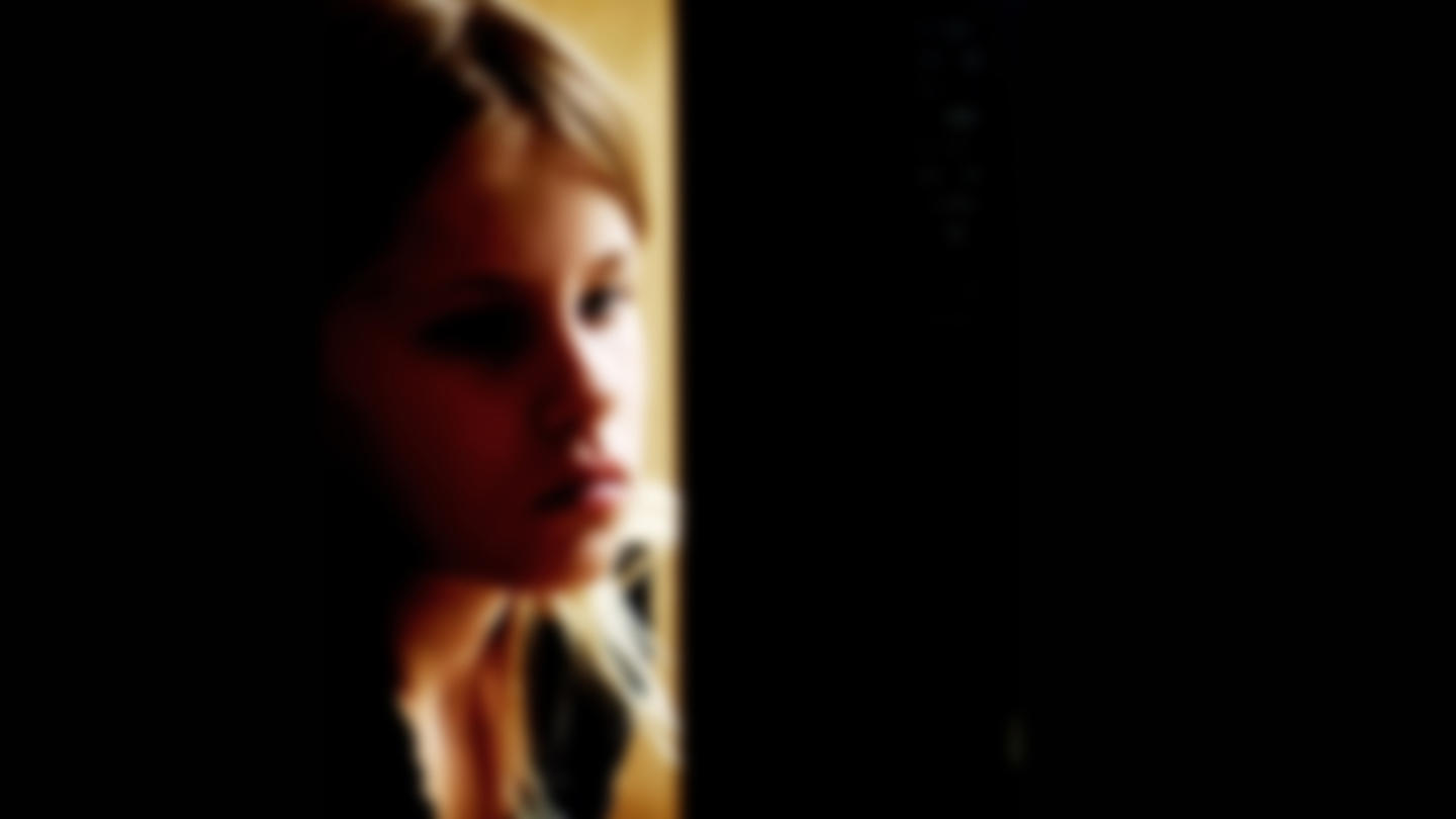 A child stares blankly in a low-lit room