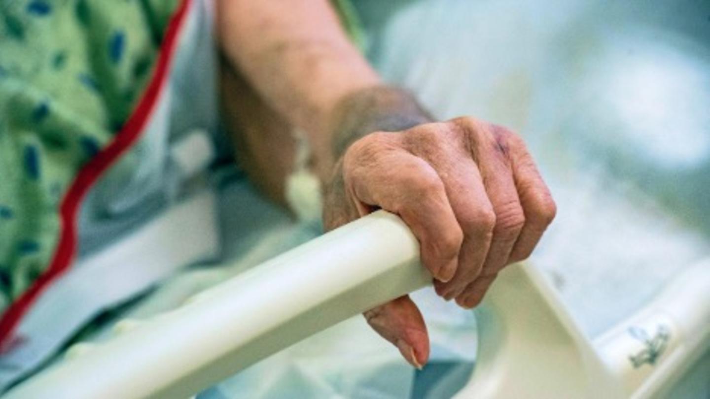 A person grasps a handrail on a hospital bed