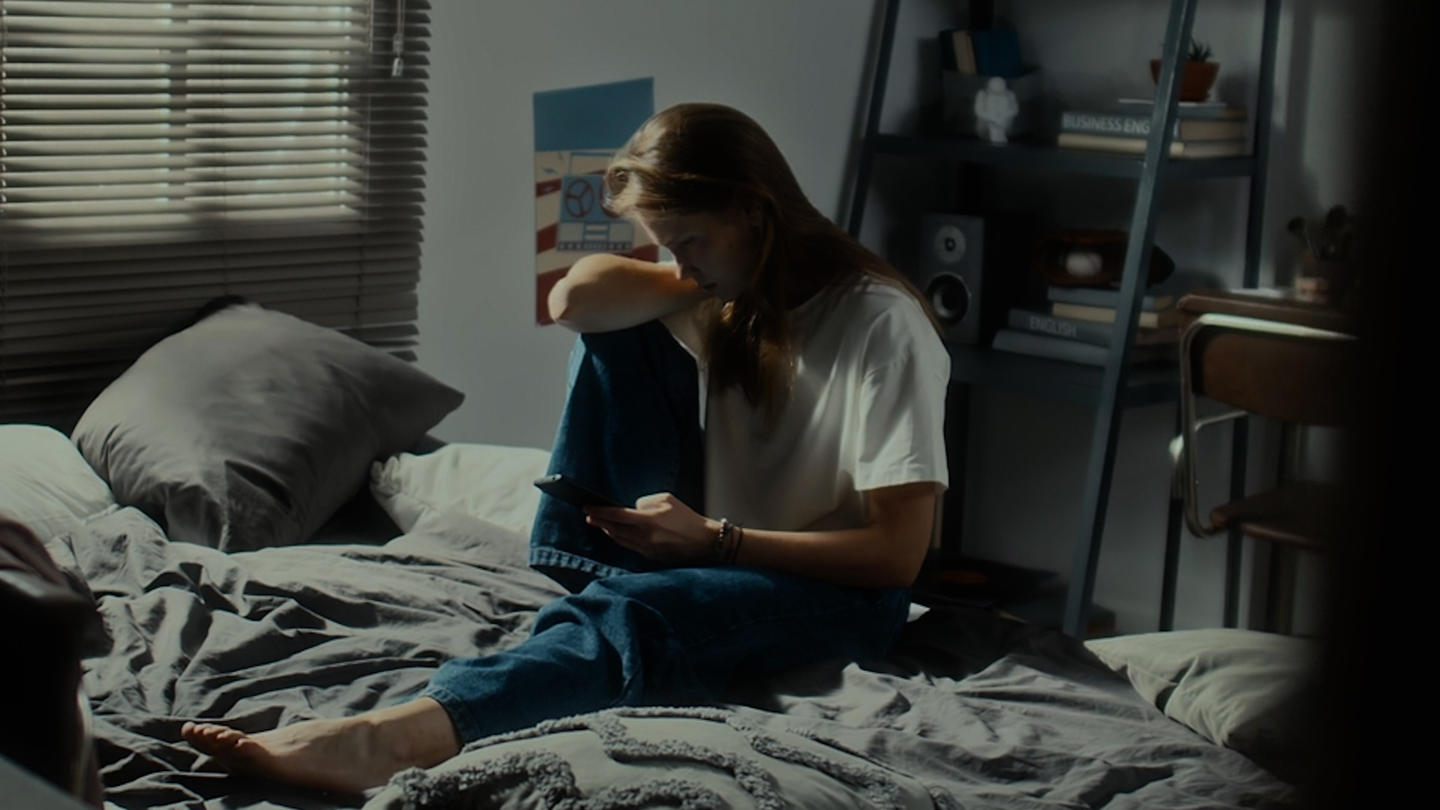 A woman sitting in a low-lit bedroom looking at her phone