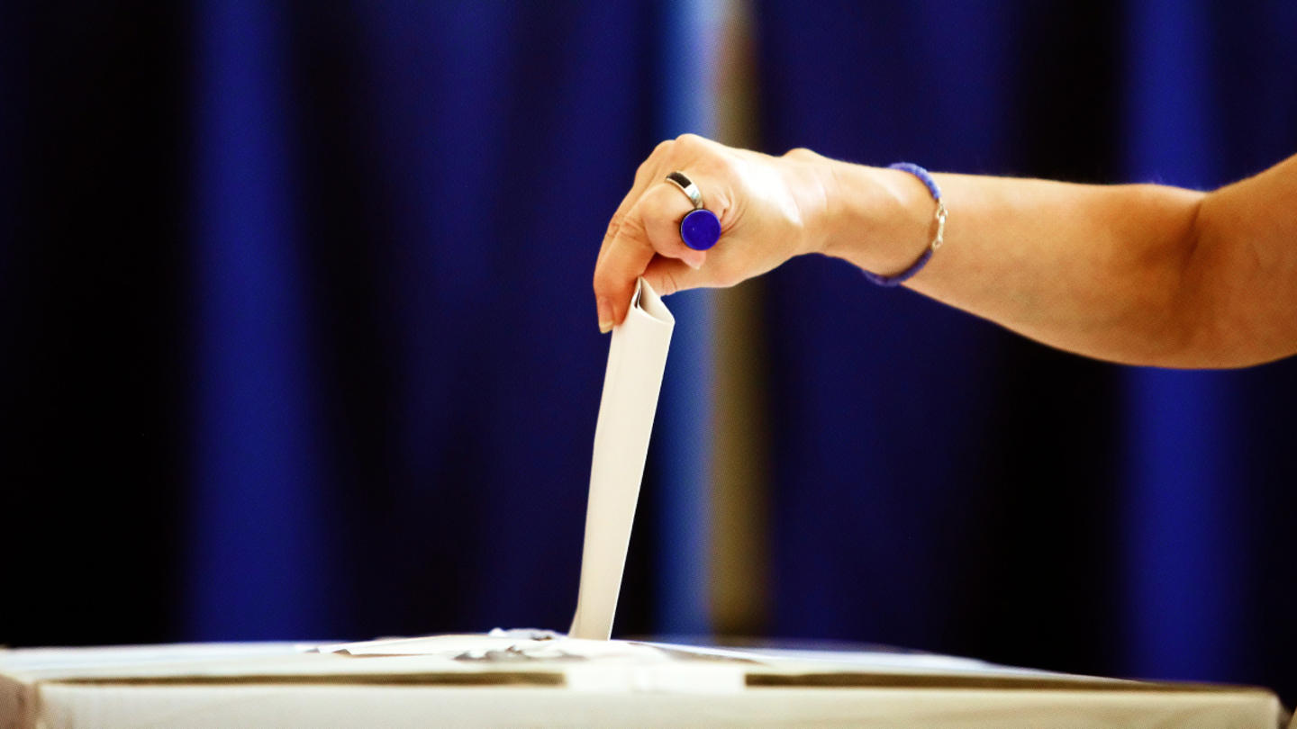 A hand picking up a piece of paper on a desk with navy background