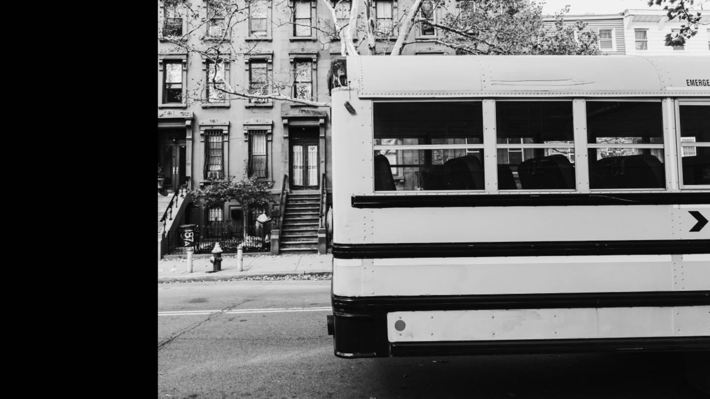 A black and white photo of a schoolbus in front of a school