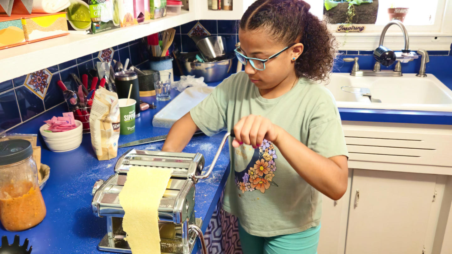 A young girl with glasses and curly hair making pasta