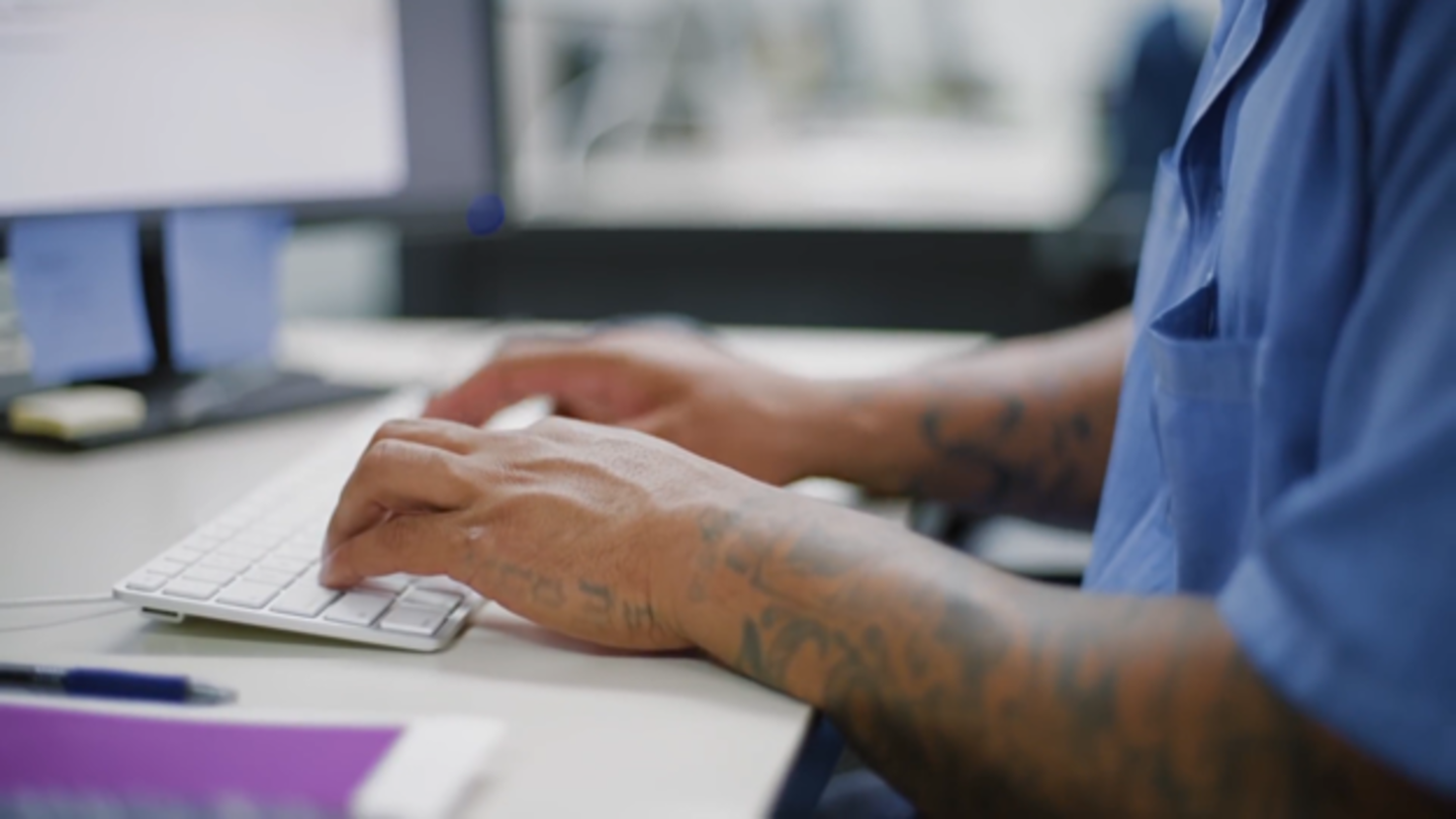 Former inmate with tattooed arms typing on a keyboard, participating in a reentry program to support their transition back into society.