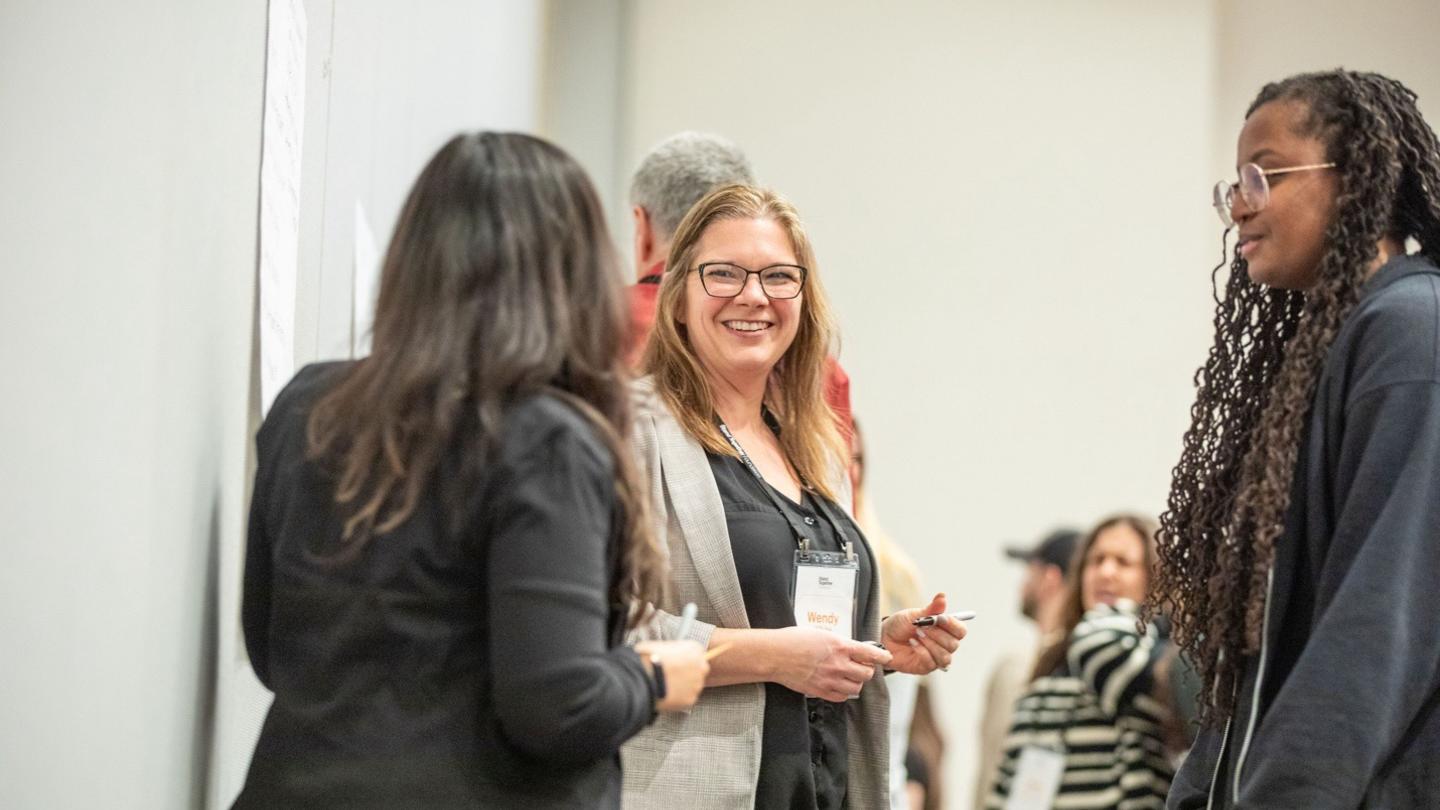 Three professionals discussing the future of work at a conference, wearing name badges and engaging in conversation