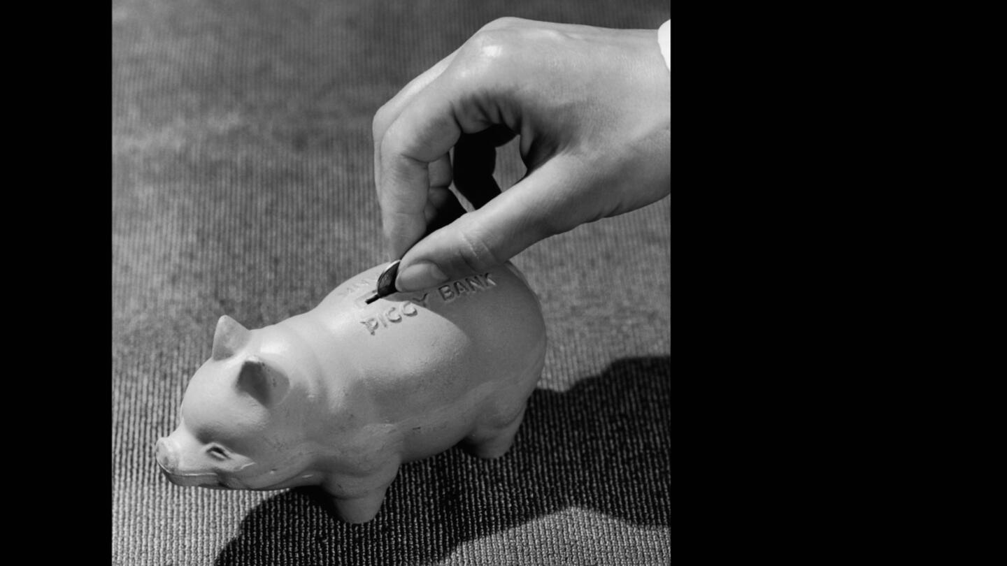 A hand putting a coin into a piggy bank. The photo is black and white