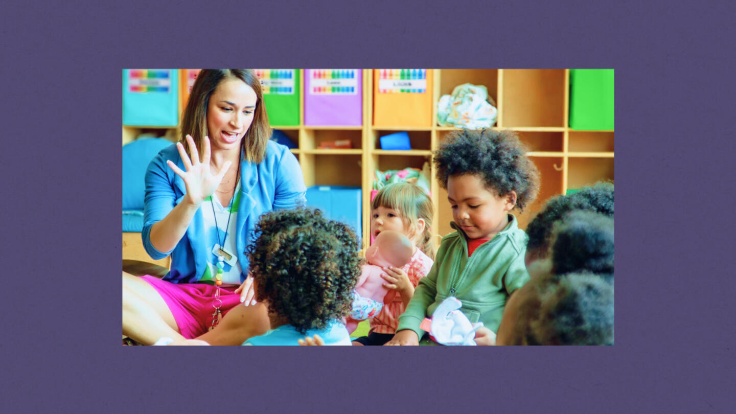 A female teacher in a blue top instructing a group of four young students in a colorful classroom setting