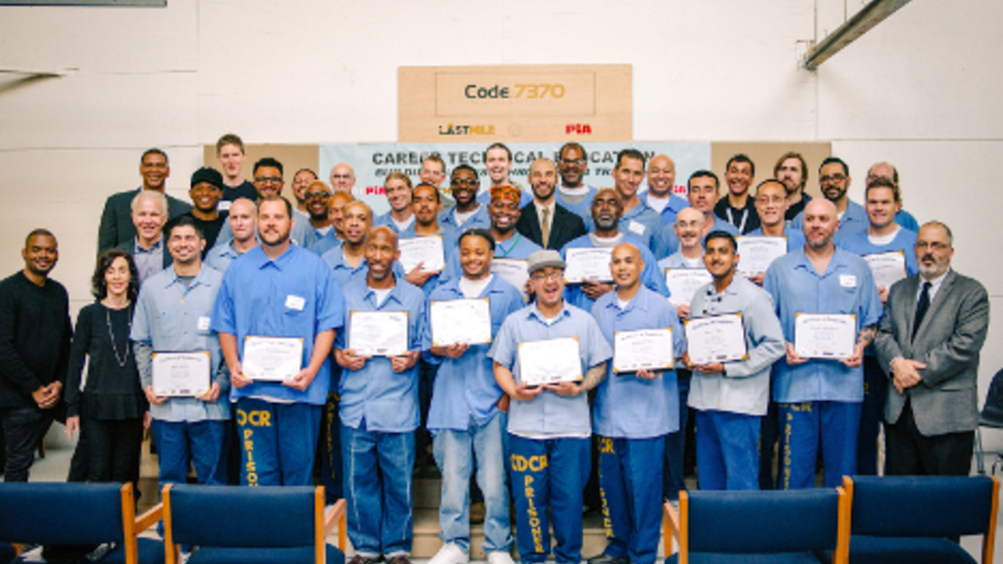 Graduation ceremony at The Last Mile program, featuring smiling formerly incarcerated individuals holding their certificates.