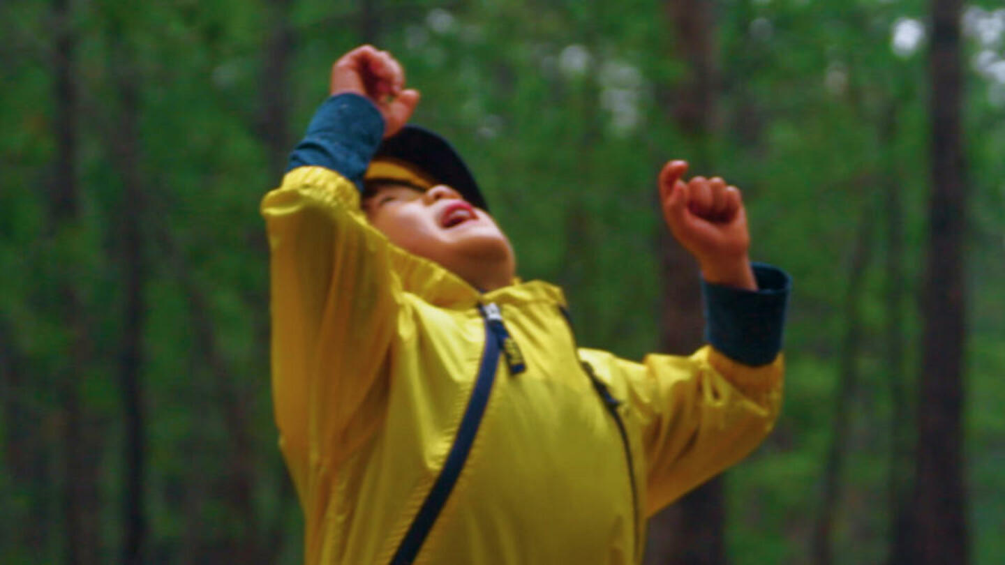 A boy playing in the rain in a yellow raincoat