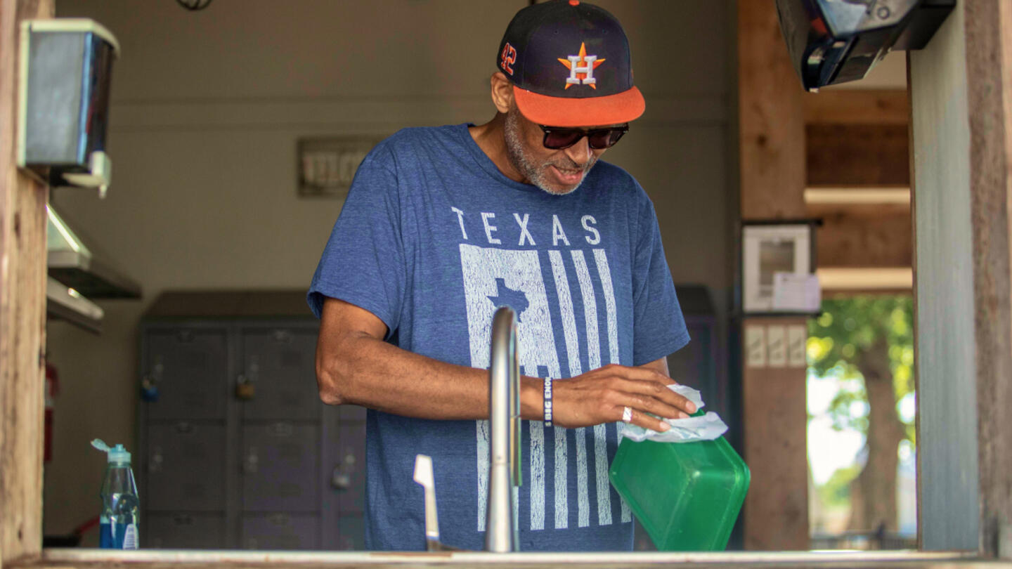A man wearing a black and orange baseball cap, blue tee shirt, and sunglasses