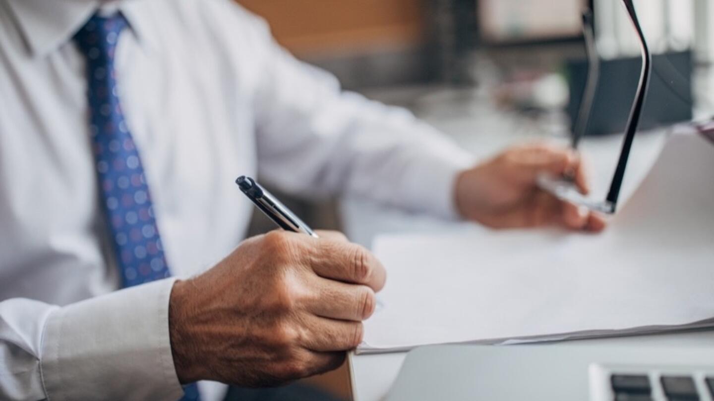 A professional in a dress shirt and tie reviews documents at a desk.