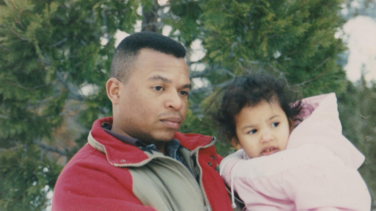 A vintage photo of a man in a red jacket holding a young girl in a pink jacket