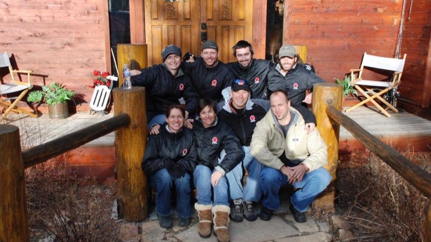A group from The Phoenix, a nonprofit that combines physical fitness and a supportive community to treat trauma and recovery, sits together in front of a wooden lodge.