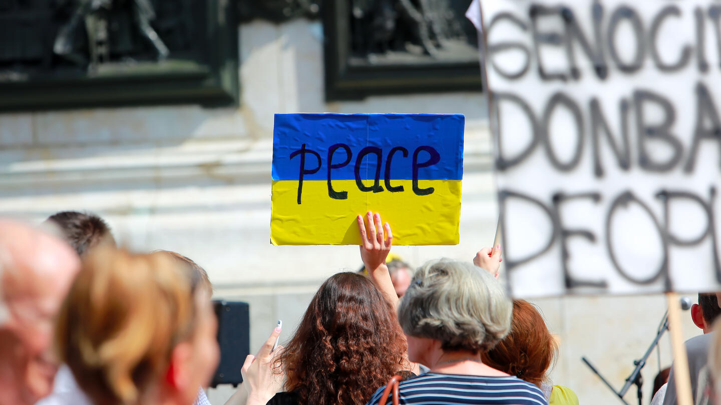 Woman holding a blue and yellow sign that says peace.
