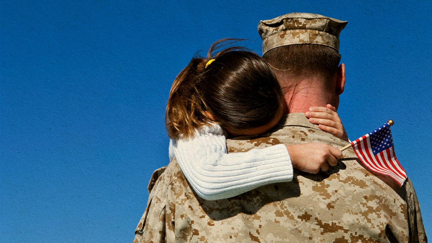 Soldier hugging a child holding an American flag.