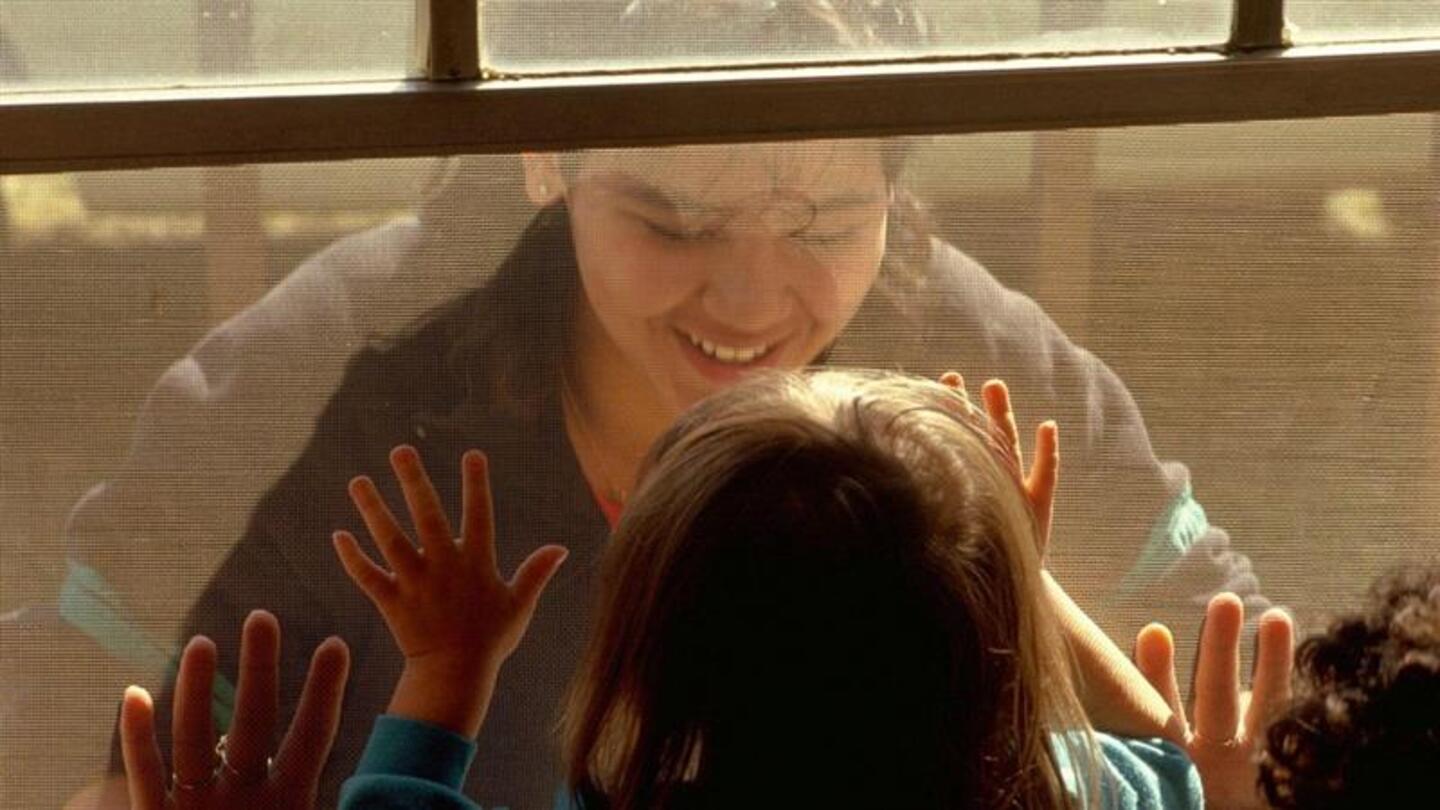 A smiling mother looking through the window at her children.
