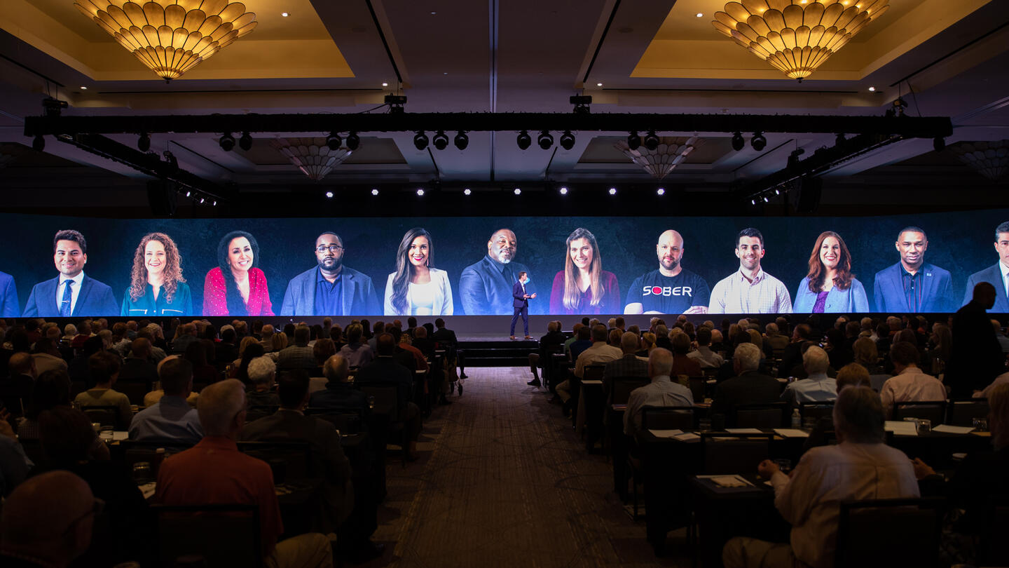 Brian Hooks speaks on stage with other summit speakers displayed behind him on a screen