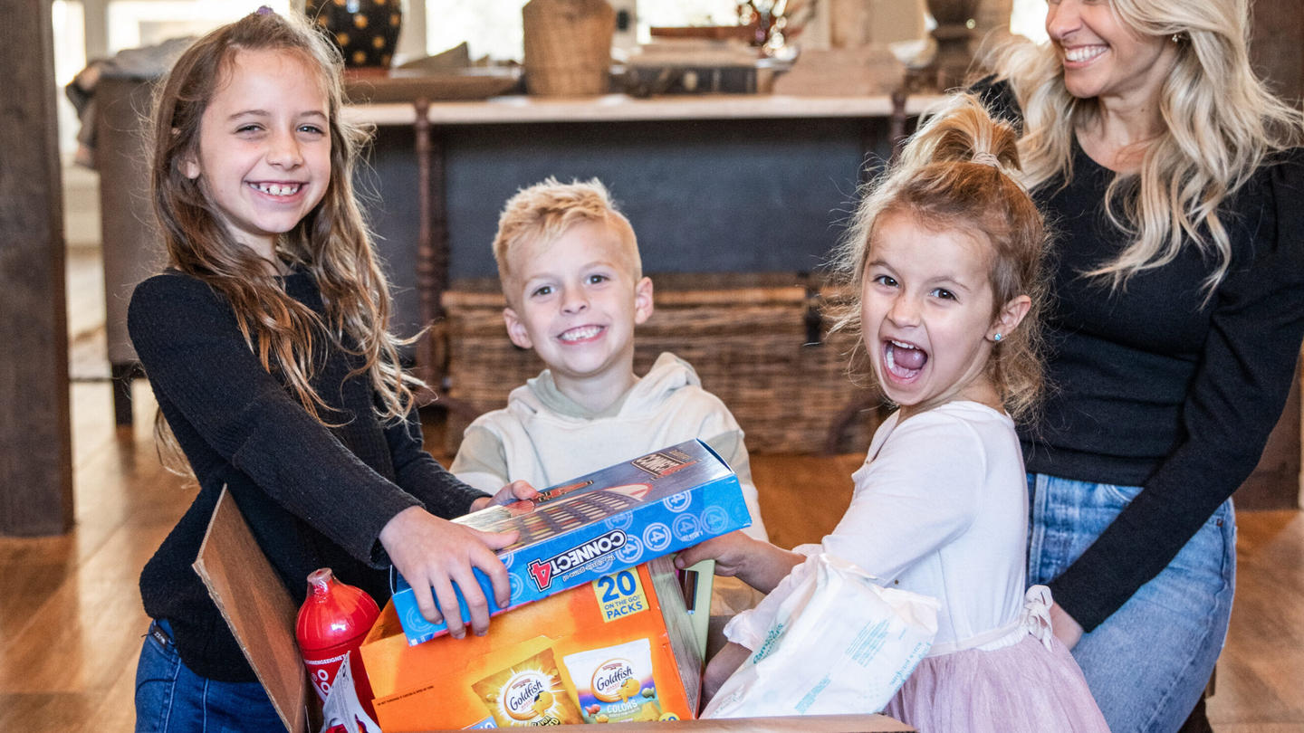 children and a women smiling for a photo as they take toys out of a box
