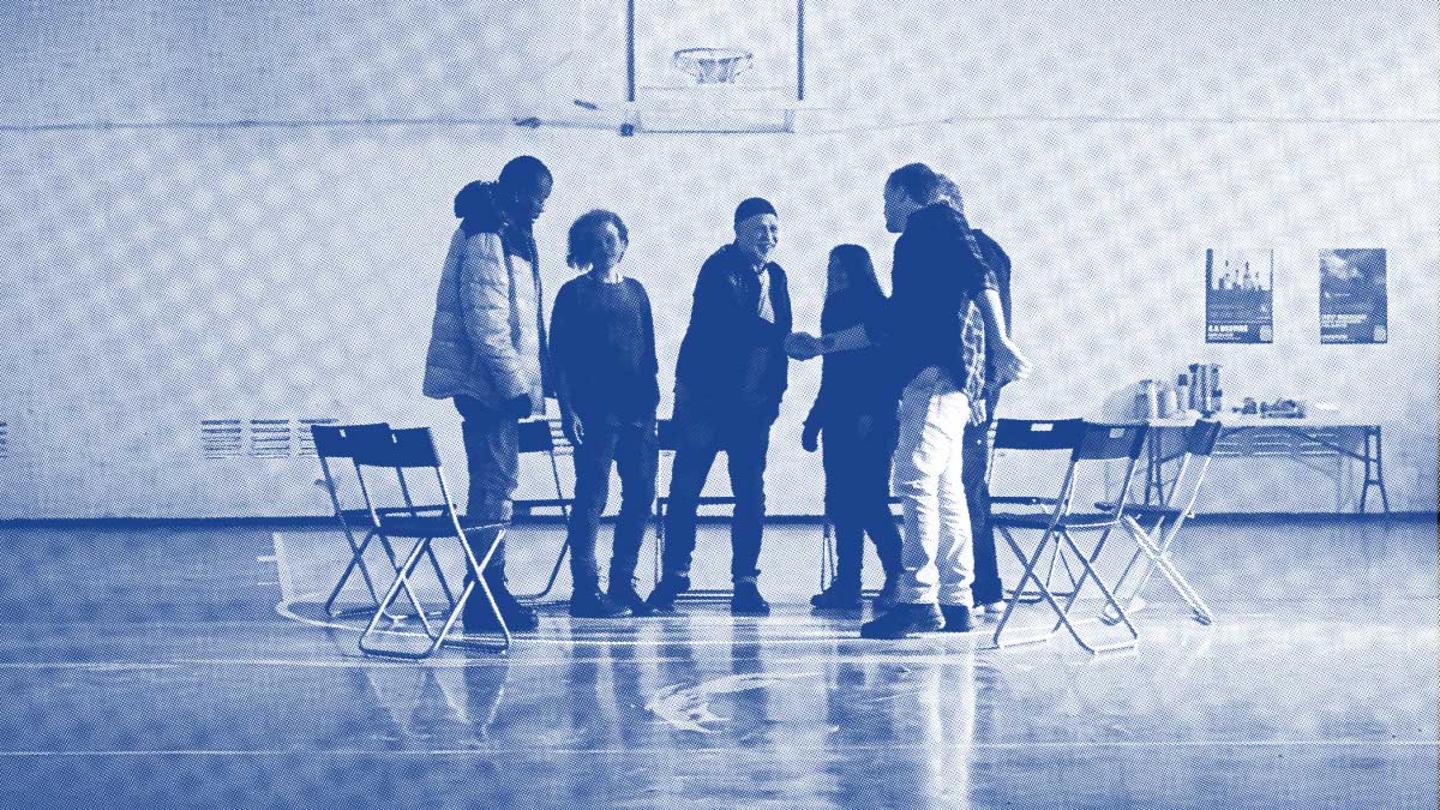 A group of people standing and conversing in a gymnasium with chairs and a table set up nearby, all in a monochromatic blue filter.