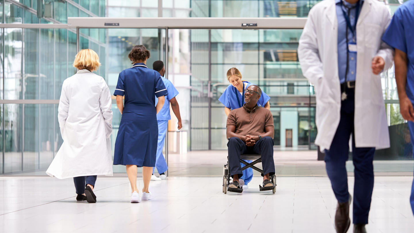 A nurse pushes a man in a wheel chair in a hospital
