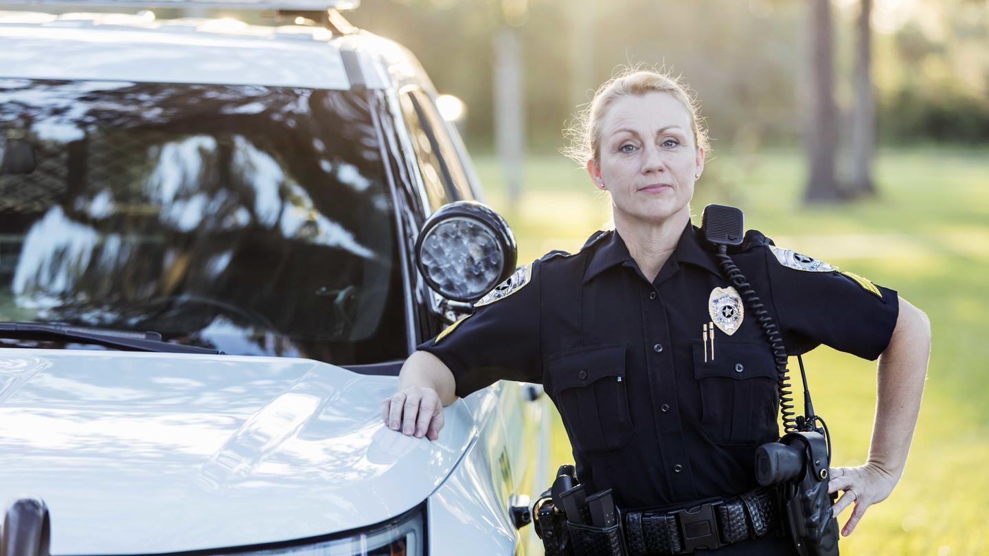 A police officer leans on her squad car, posing for a photo