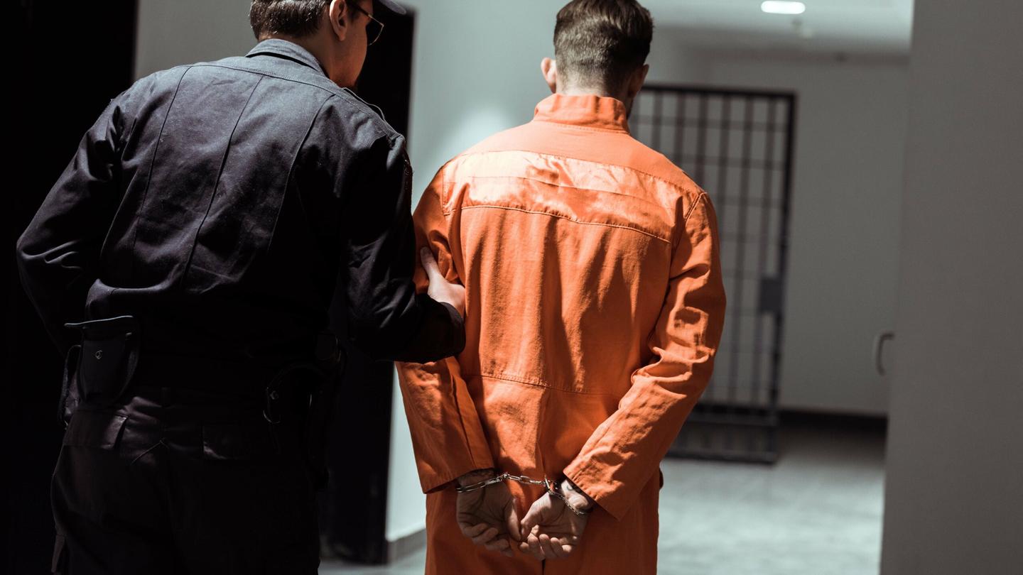 A corrections officer guides an inmate through a correctional facility