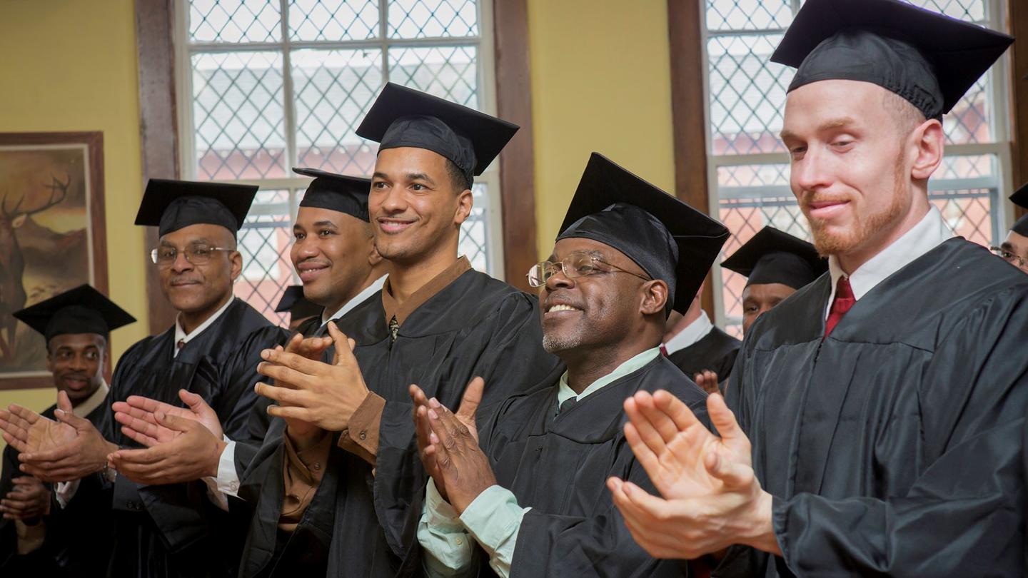 A group of men wearing caps and gowns clapping and smiling