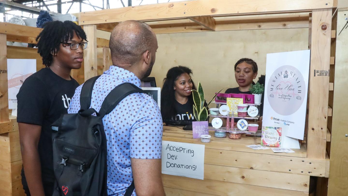 A man and a teen approach a booth set up by two young entrepreneurs