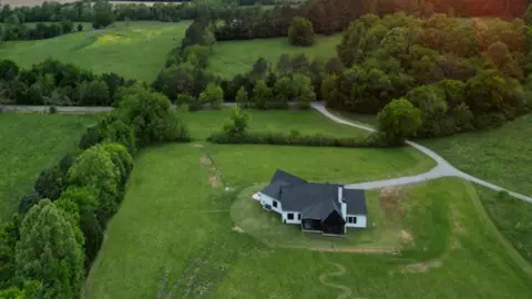 An aerial view of a white home surrounded by green fields and trees