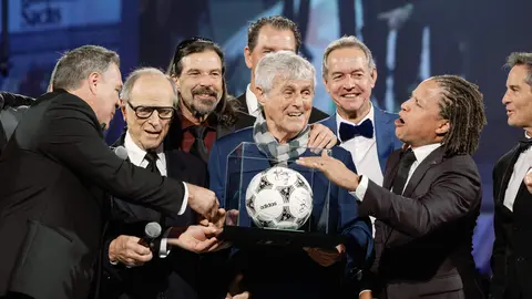 Group of men on stage presenting a signed soccer ball in a display case during an awards ceremony.